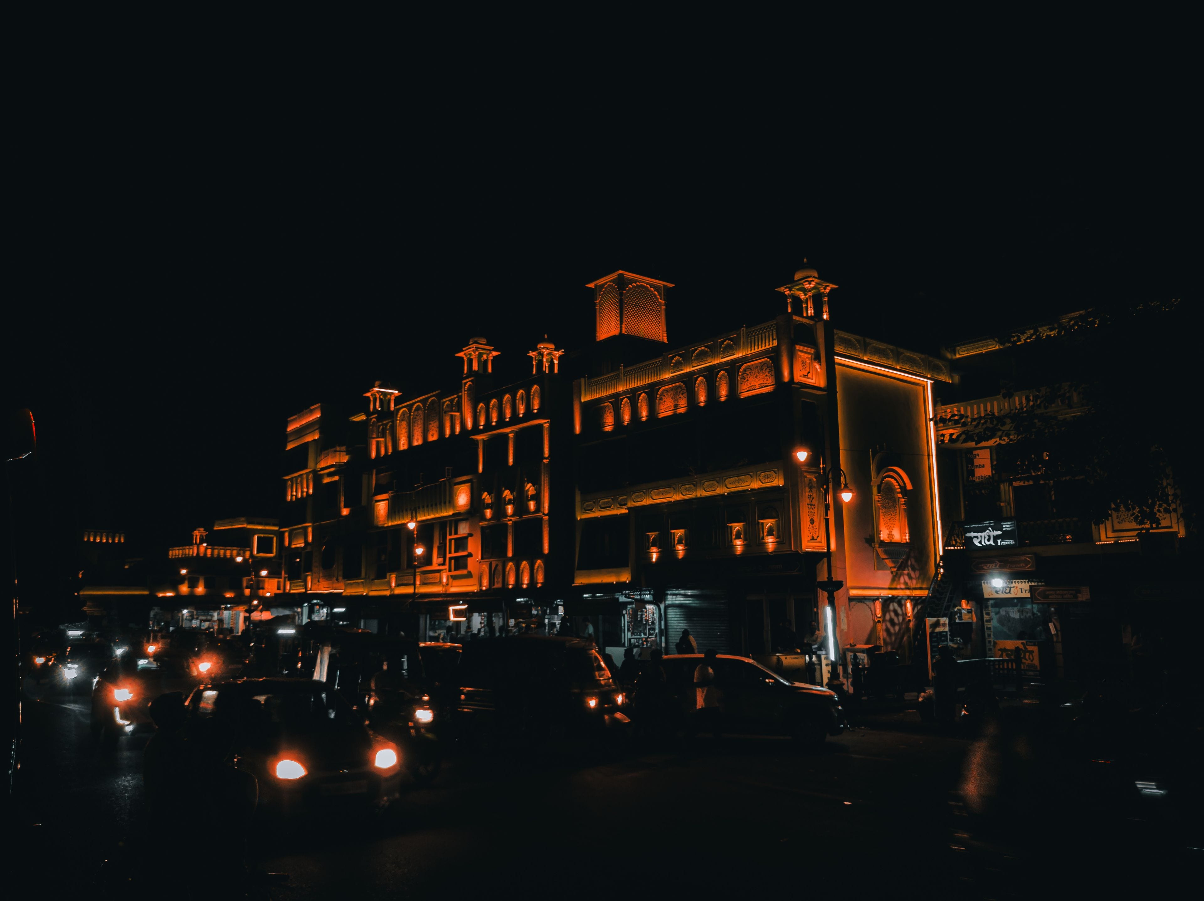 An Indian street at night, a lit heritage building and traffic, shops still open