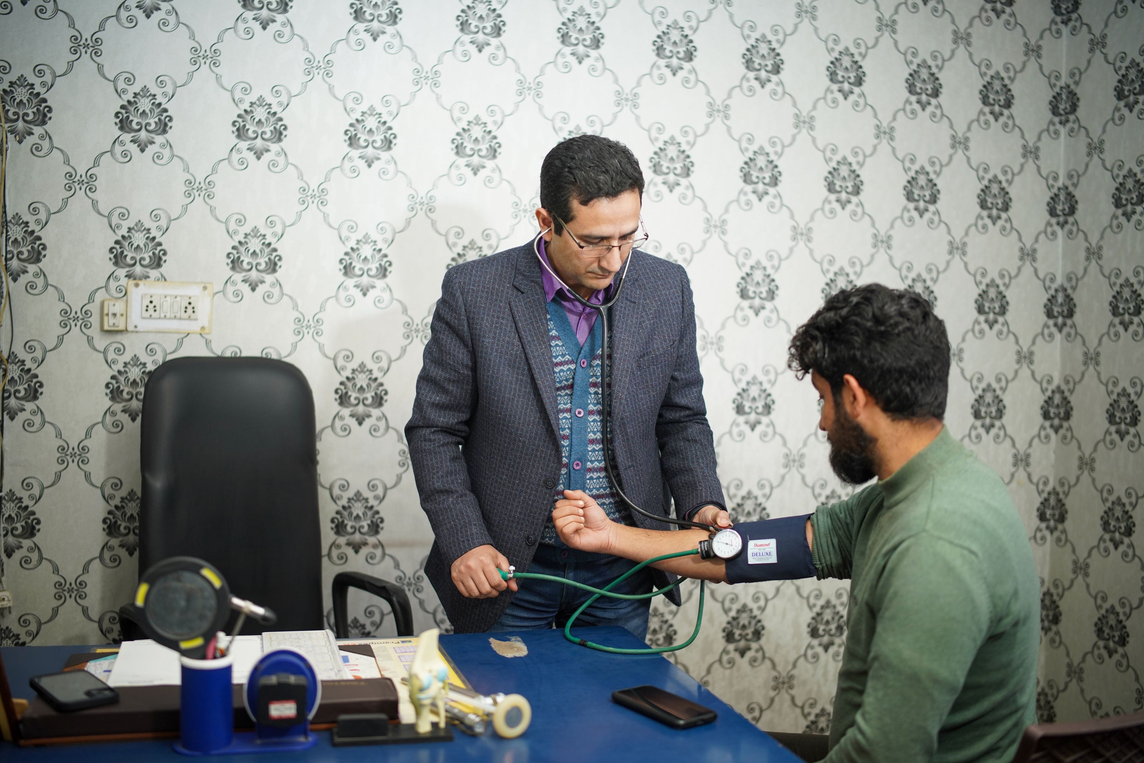 A doctor taking a patient's blood pressure in an Indian outpatient consulting room